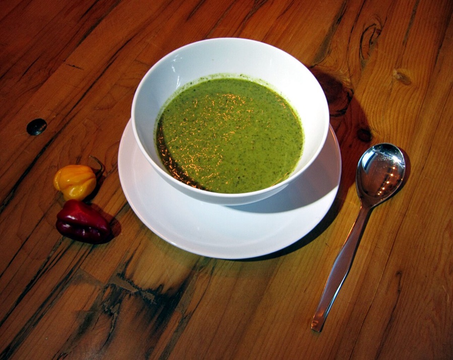 A bowl of green velvet callaloo with peppers beside
